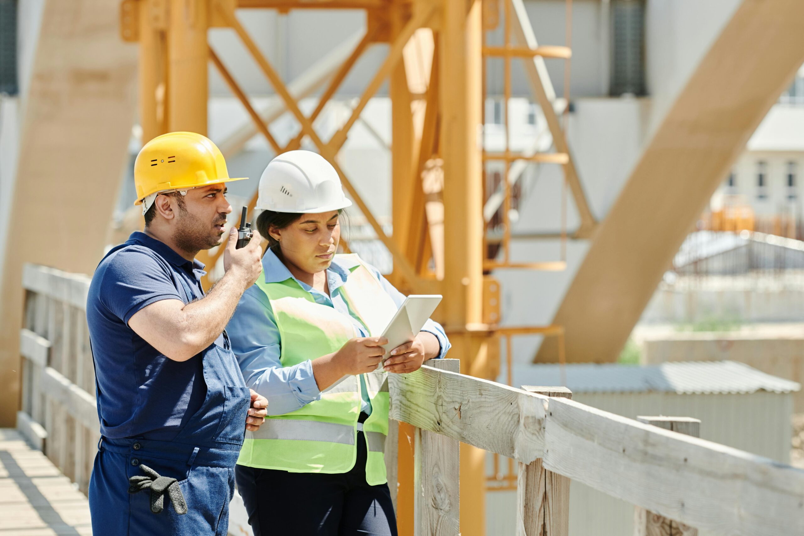 Two field engineers wearing safety gear reviewing inspection data on a tablet at an industrial site.
